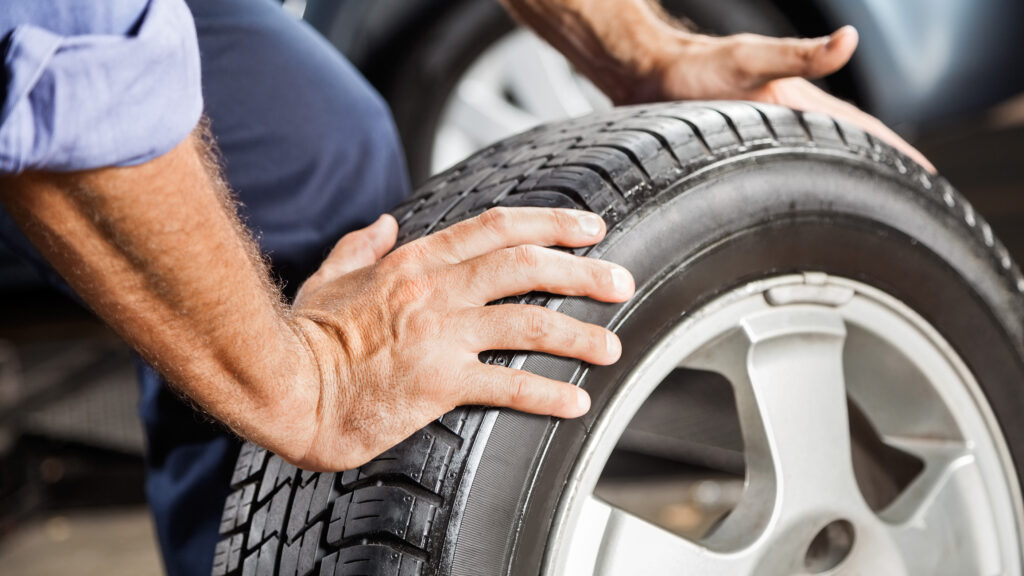 Close-up of a person’s hands inspecting a car tire, focusing on the tread and sidewall.