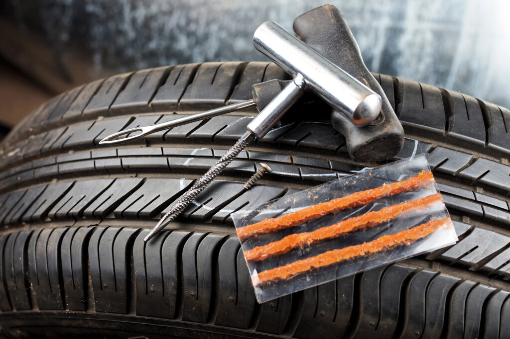 A tire plug repair kit is displayed on top of a tire, including a T-handle tool, a reamer, and rubber plug strips.