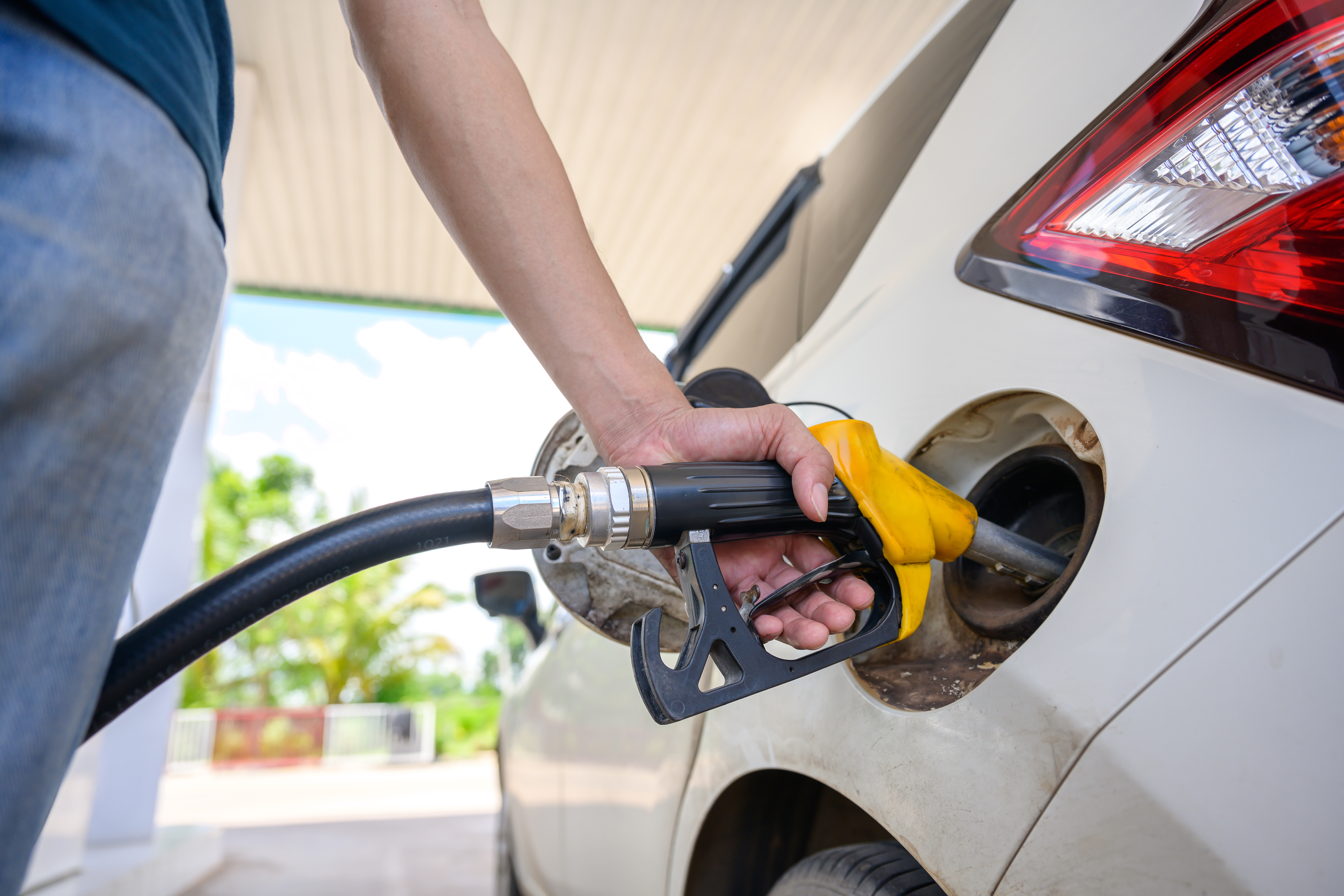 A close-up of a person using a yellow fuel nozzle to fill up their car at a gas station. of energy-related projects, the fuel industry, daily convenience, and transportation