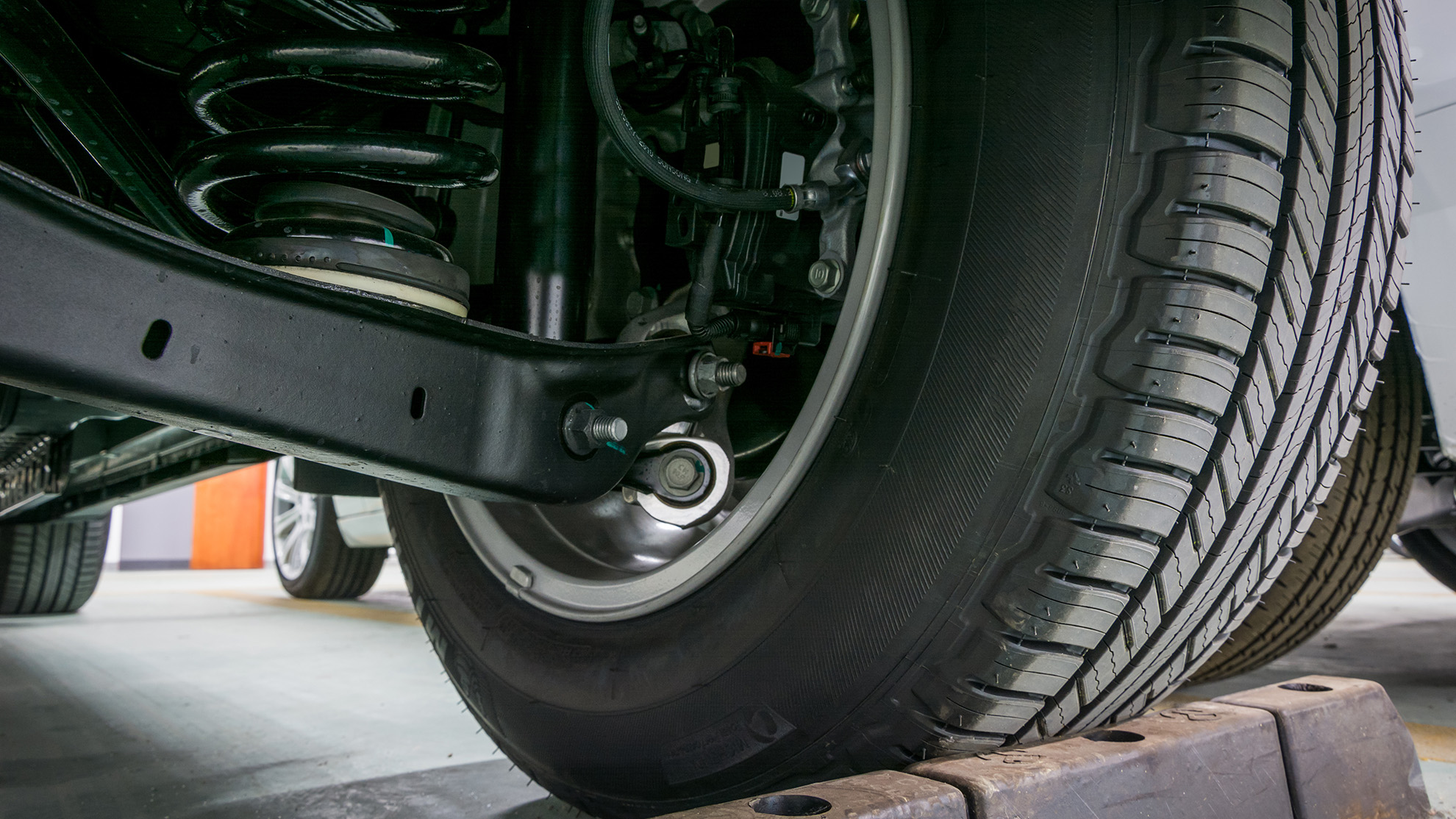 Close-up view of a car’s suspension system and rear wheel, highlighting the coil spring, shock absorber, and tire tread.