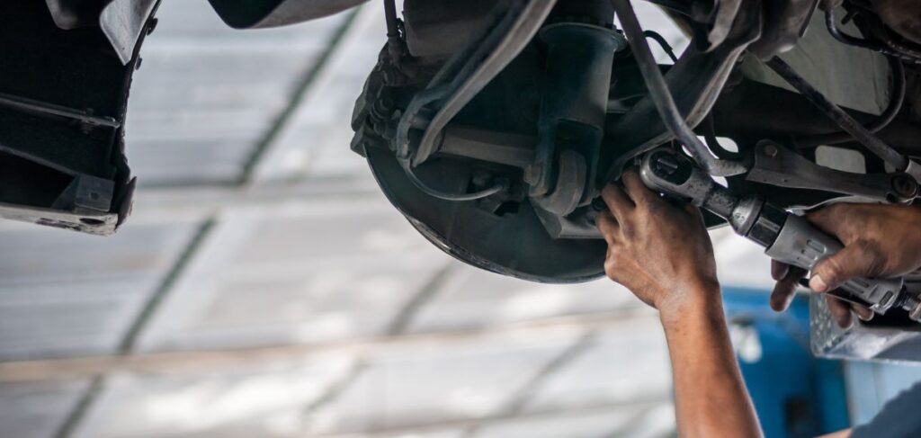 Mechanic working under a vehicle, using a power tool to repair or replace suspension components.